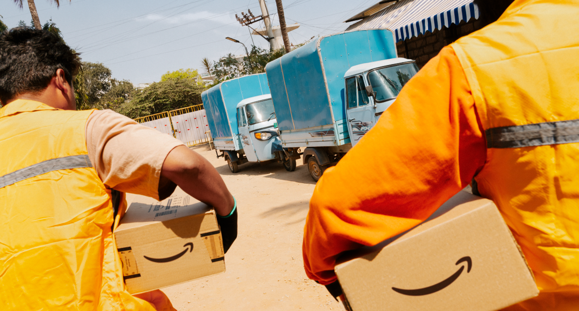 Two people in orange vests carrying Amazon packages. 