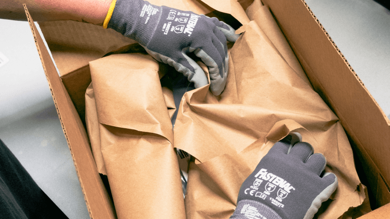 Hands are shown placing packaging material inside a cardboard box. 