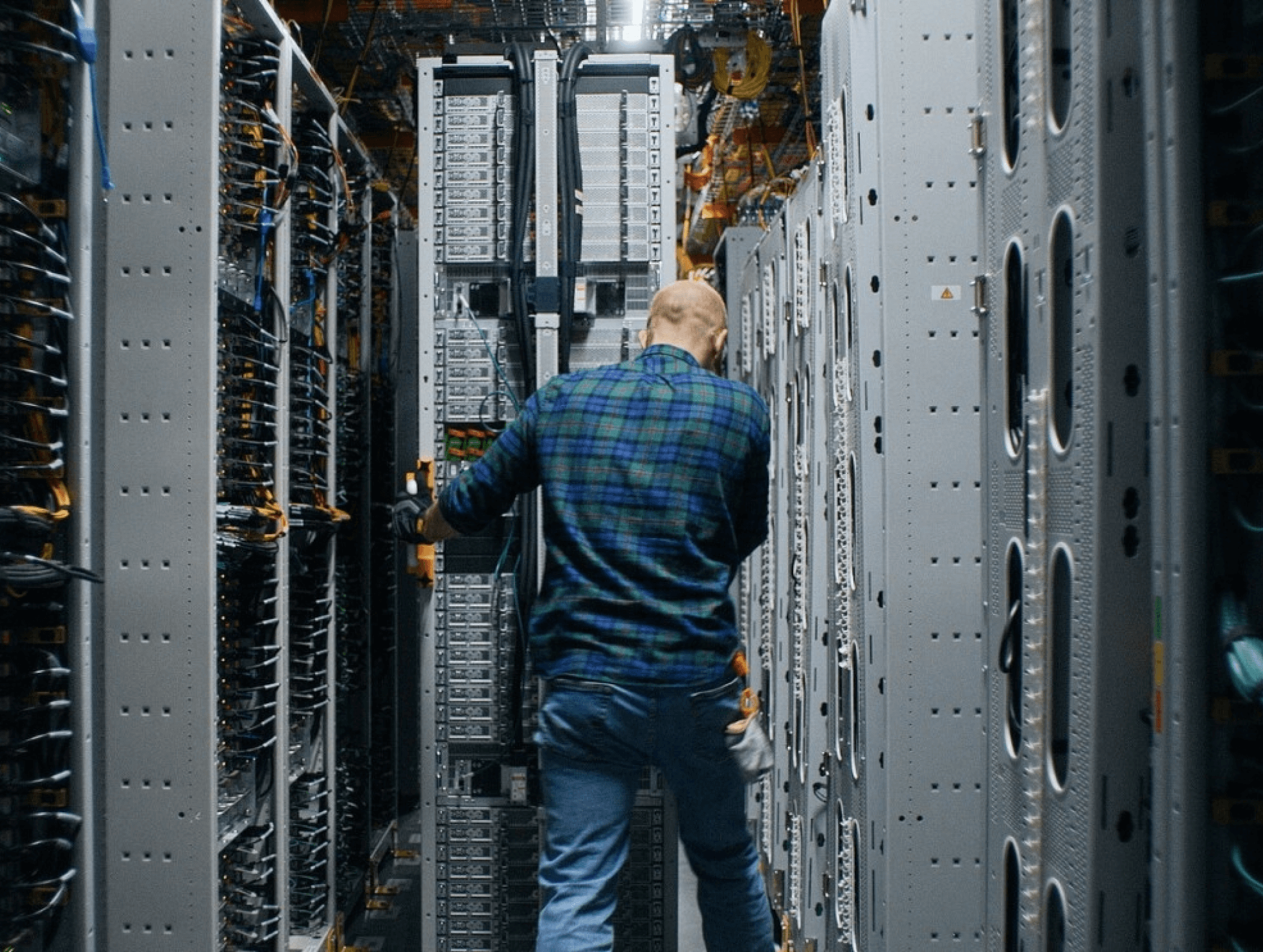 A person wheels a box of computer equipment down rows of server hardware. 