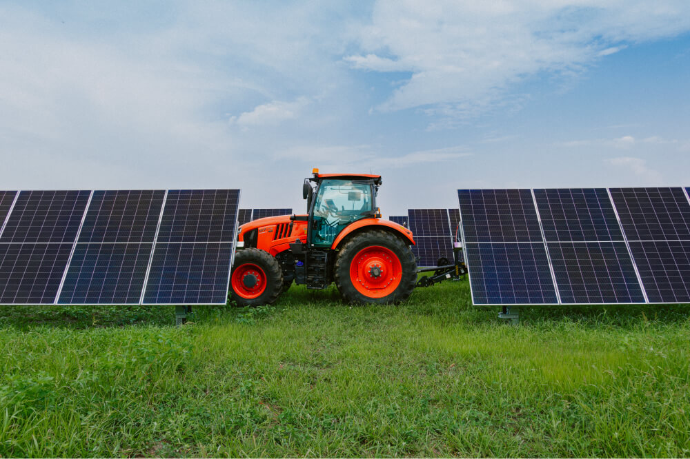 A tractor drives in front of rows of solar panels in a green field.