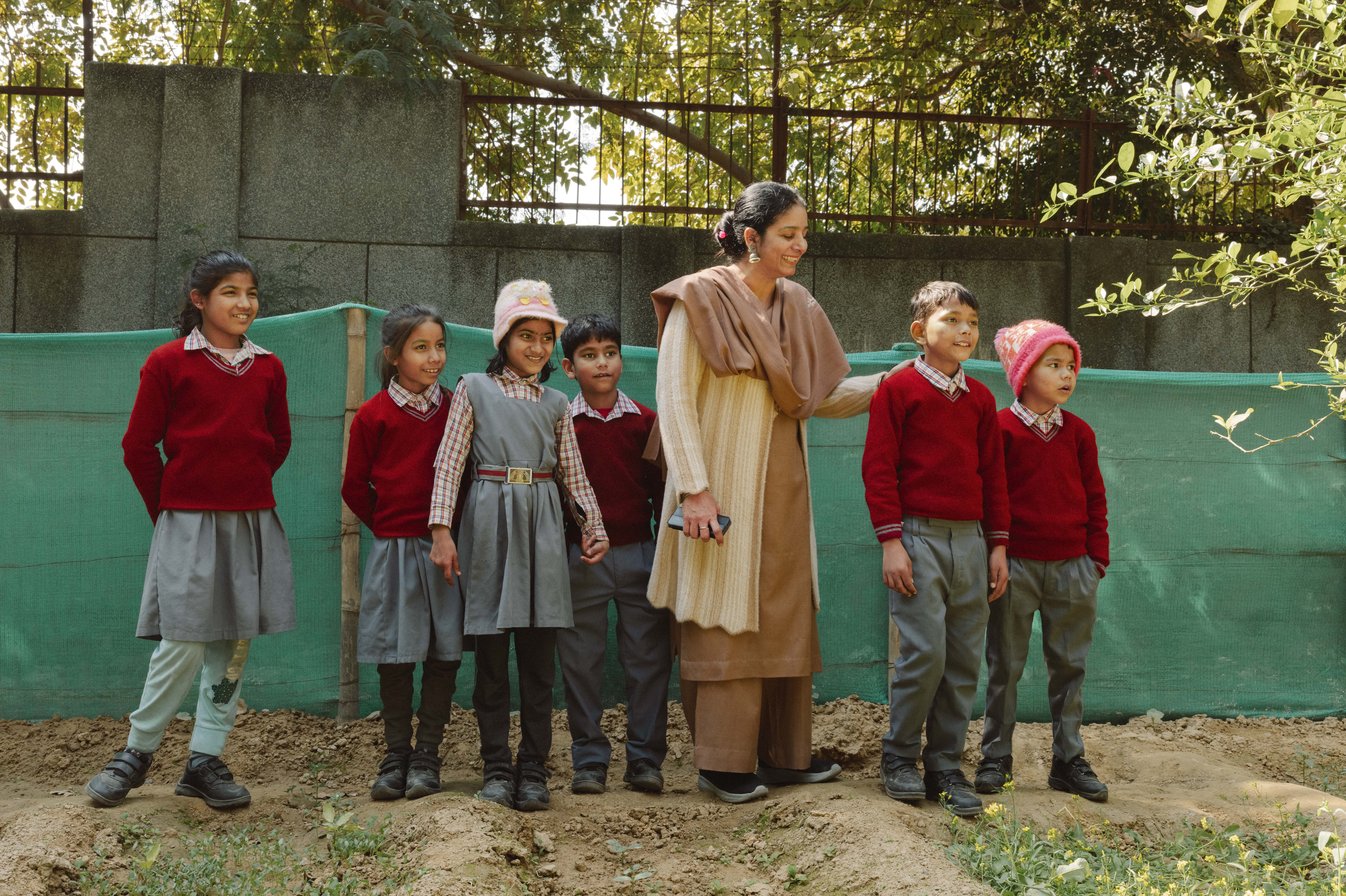A group of school children stand with their teacher in a school garden.