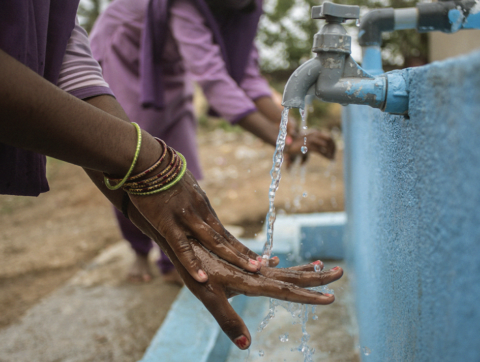 Two people wash their hands in water basins.