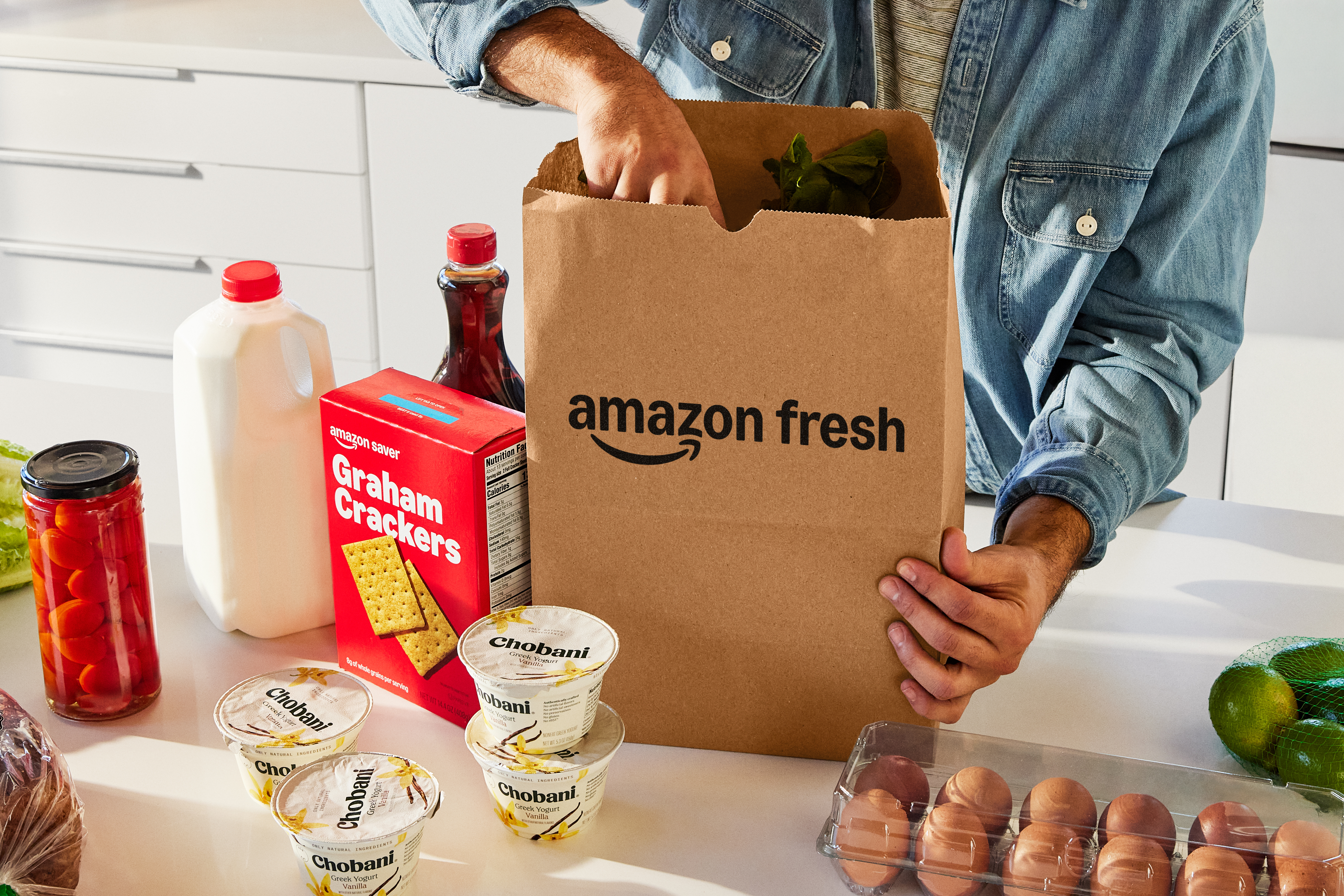 A person takes groceries, including yogurt, milk, and eggs, out of a paper Amazon Fresh bag. 