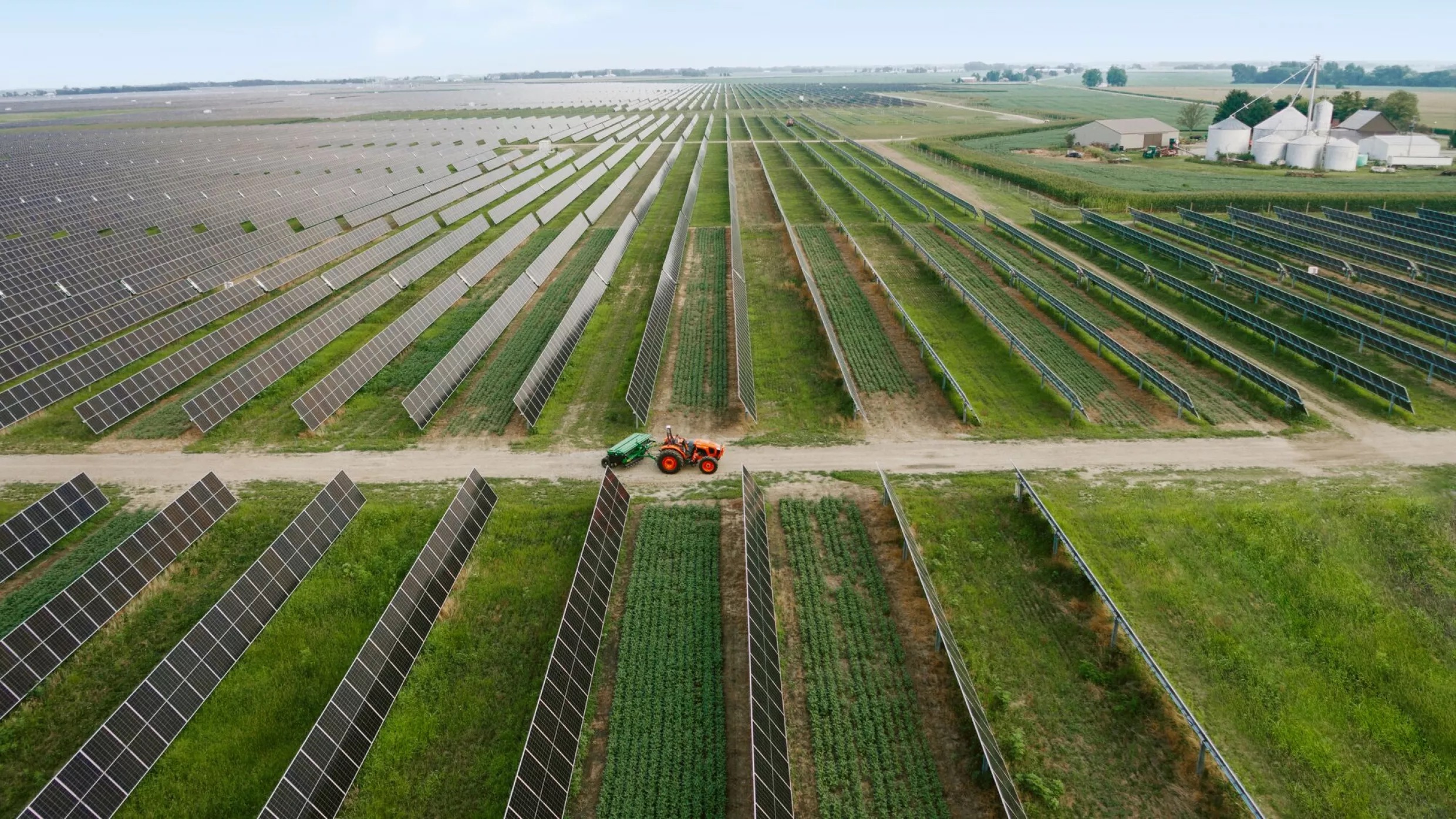 An aerial view of a tractor driving through rows of solar panels. 