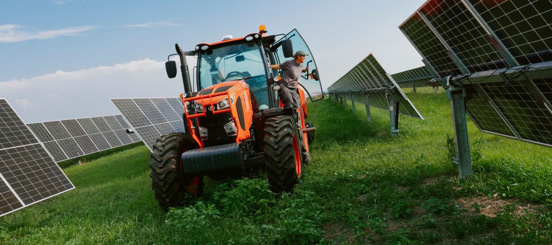 A tractor drives through a field of solar panels.