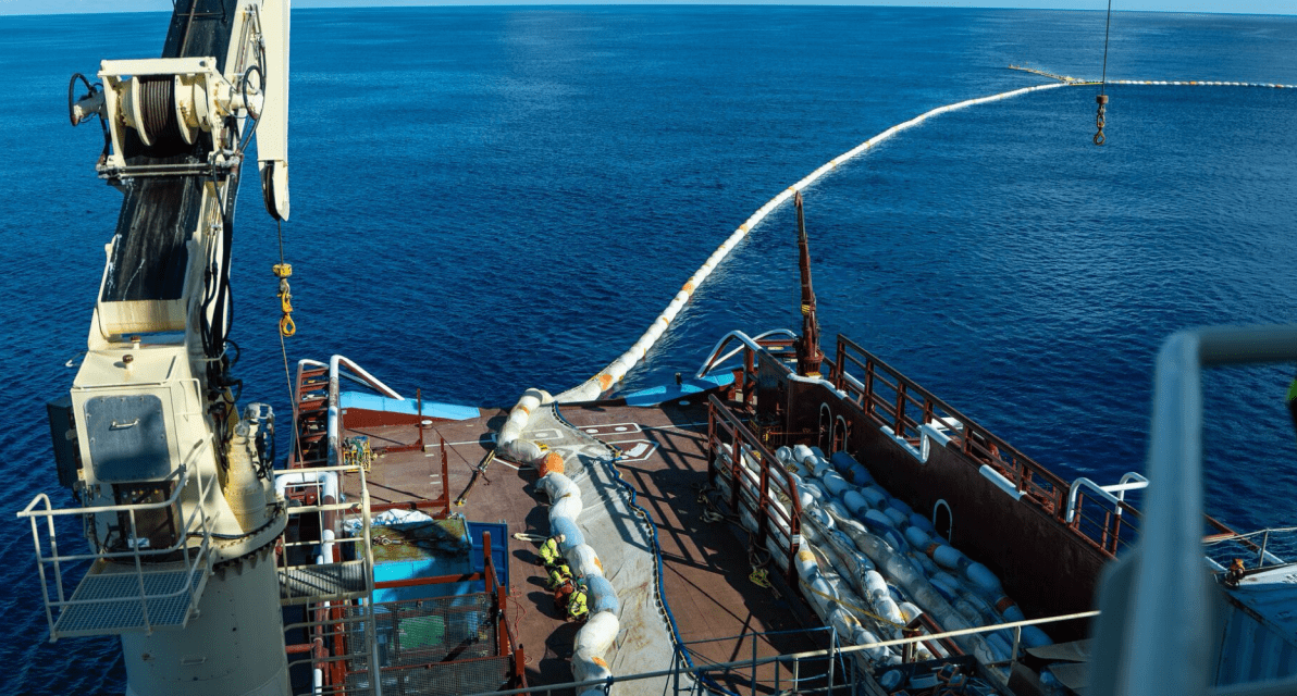 A view from the top of a ship shows buoys lining the top of a large net collecting trash in the ocean.