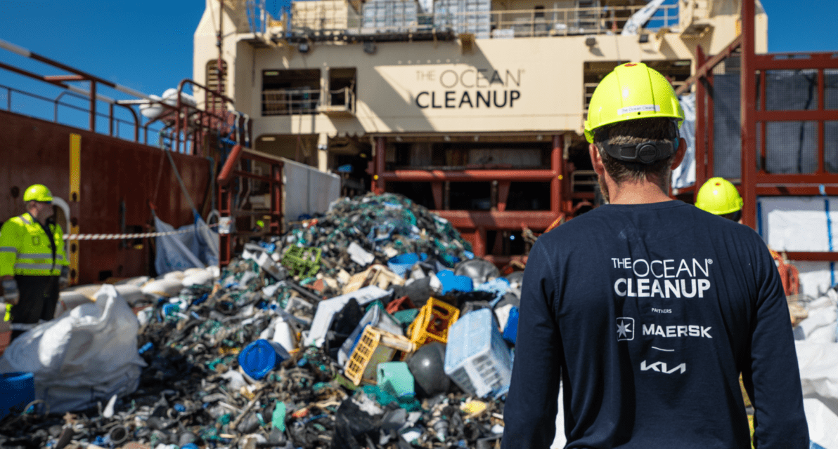 A person in a hard hat walks toward a pile of trash on a ship deck.