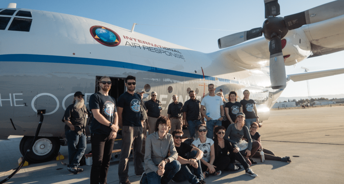 A group of people smiles in front of a plane that reads "International air response."
