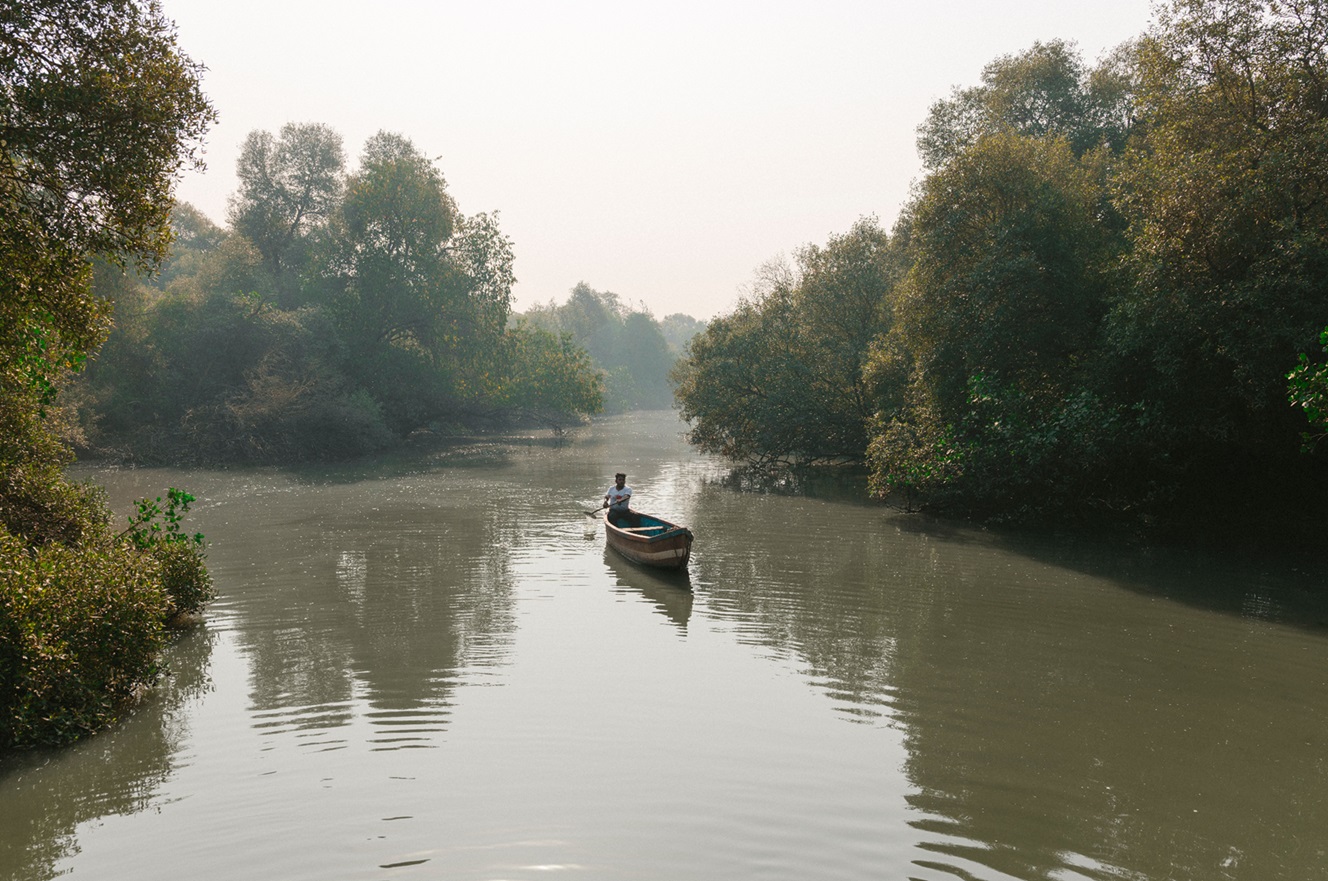 A person paddles a boat down the middle of a river. 